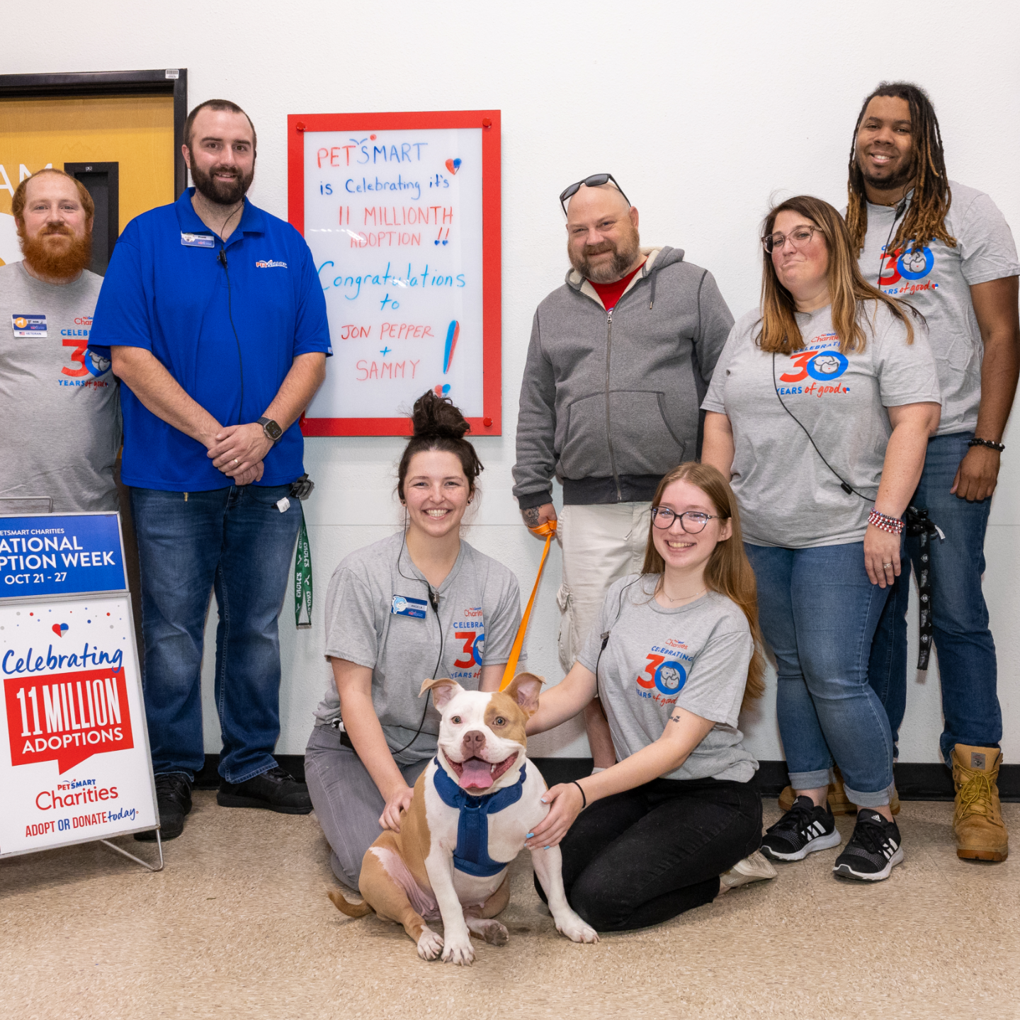 A group of PetSmart employees poses in-store with a large dog sitting in the center