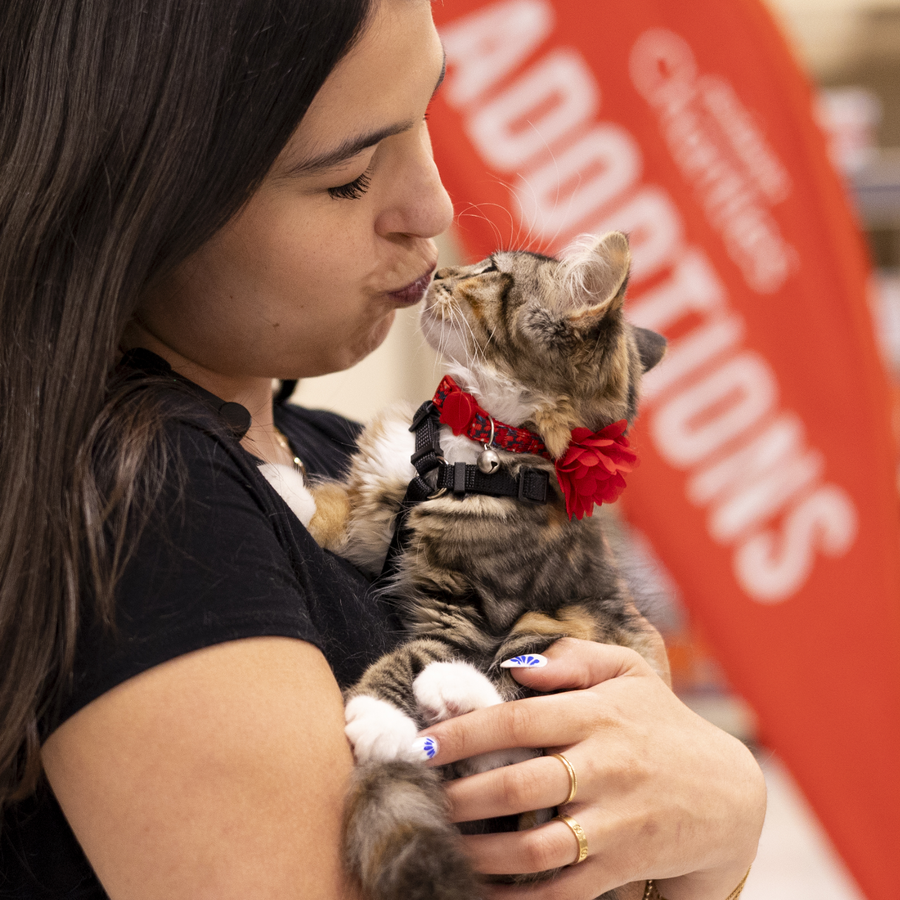 woman makes a kissy face at a kitten she's holding in her arms in front of a banner that reads "PetSmart Charities Adoptions"