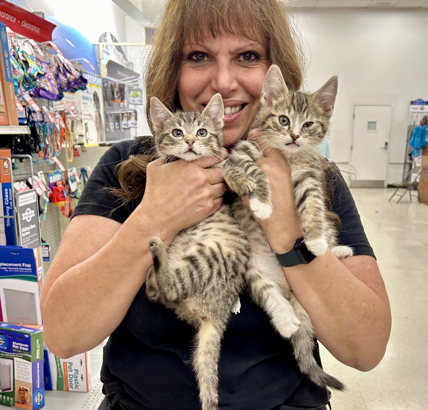 a woman smiles while holding a striped kitten in each arm