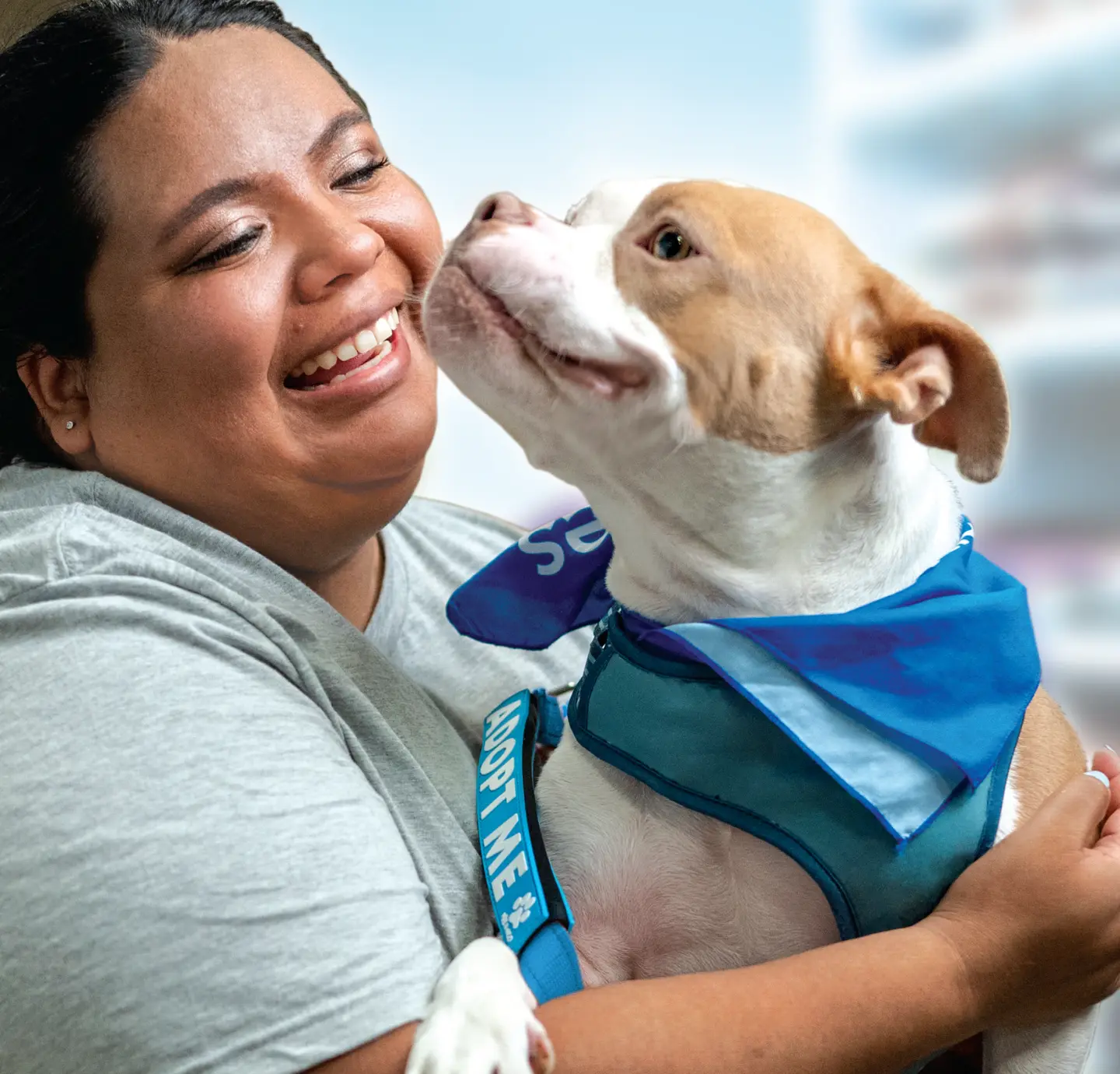 a woman smiles while hugging a dog wearing a bandana and a leash that reads "adopt me"