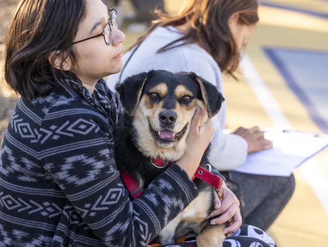 woman wearing patterned sweater sits outside with a black and tan dog in her lap