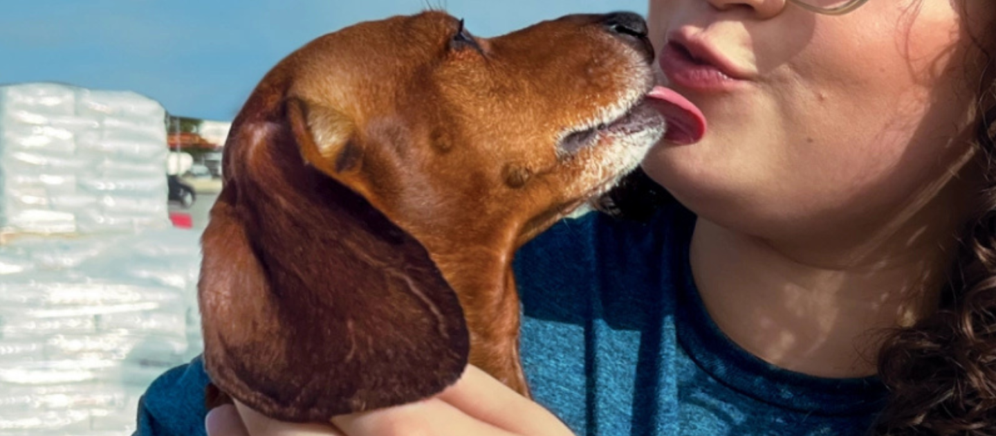 woman kisses dog in front of PetSmart Charities food bags 