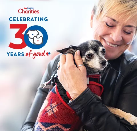 woman holds a chihuahua wearing a red sweater and PetSmart Charities' 30 years of Good Icon